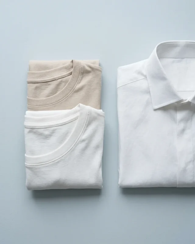 Folded white and sand undershirts beside a white shirt